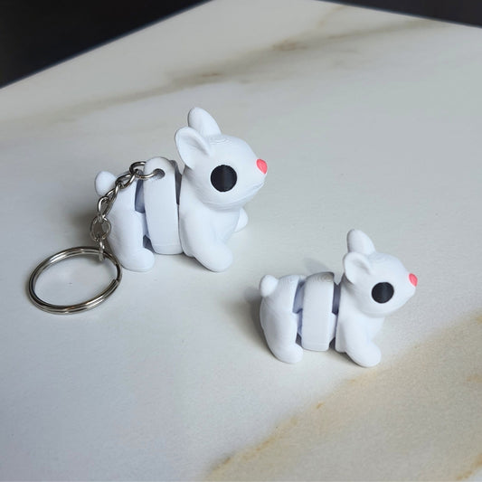 A small 3D printed white bunny keychain with black eyes and a pink nose, displayed on a marble surface.