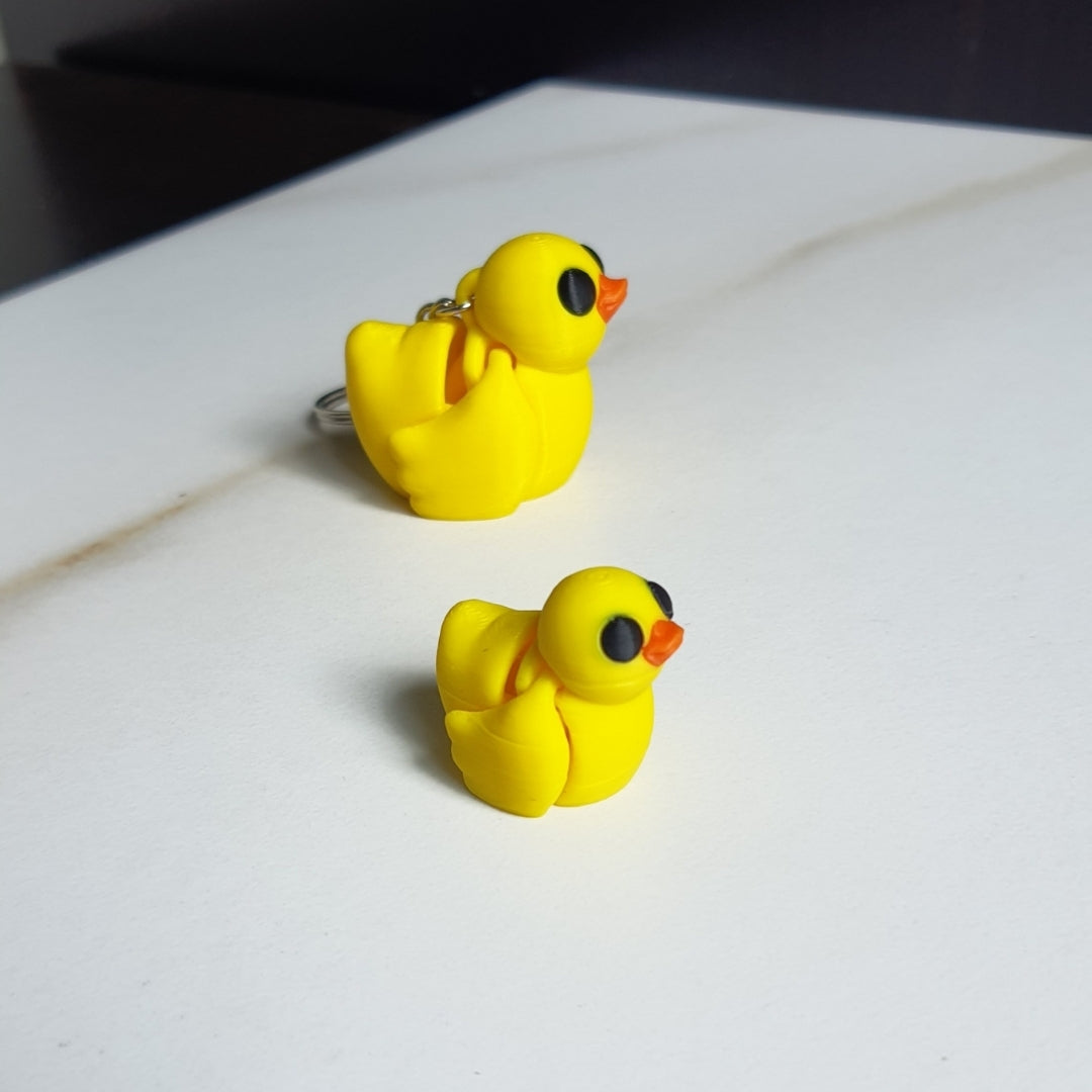 Two small, three-dimensional yellow duck toys with black eyes and orange beaks printed by Minixie, set against a white background.