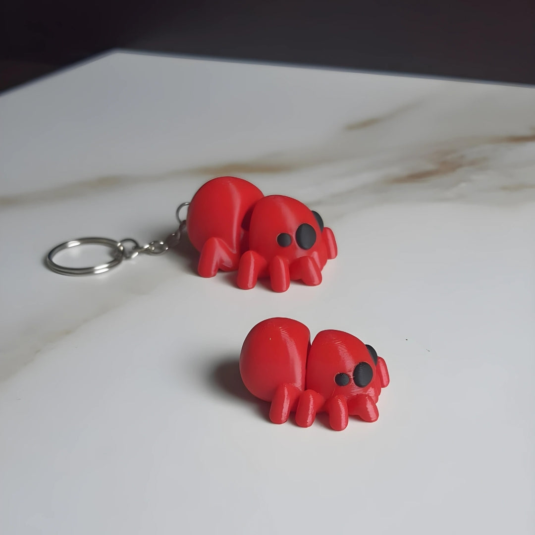 Two small 3D printed red spider with black eyes, one designed as a keychain with a metal ring, and the other a standalone figure.
