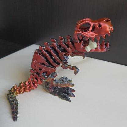 3D-Printed articulated dinosaur toy in red-gold and black colors with a glow-in-the-dark bone accessory.